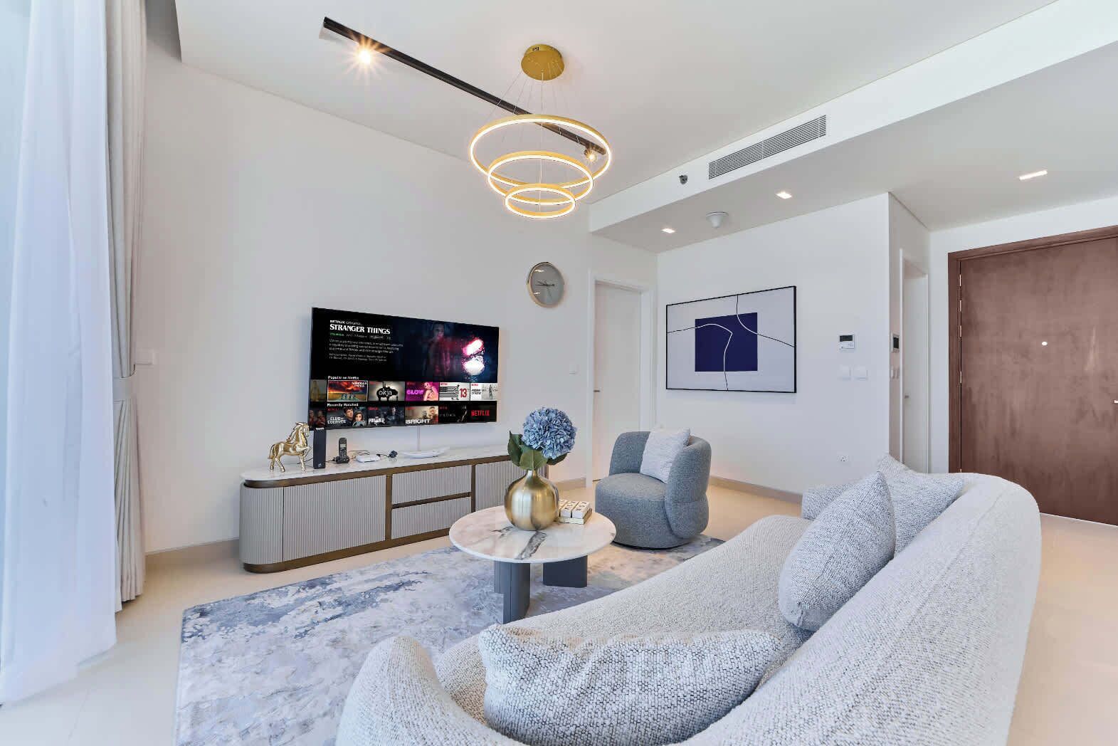 Un salon moderne doté d’un grand téléviseur à écran plat, d’une table basse ronde, d’un canapé gris et d’un style de décoration minimaliste.