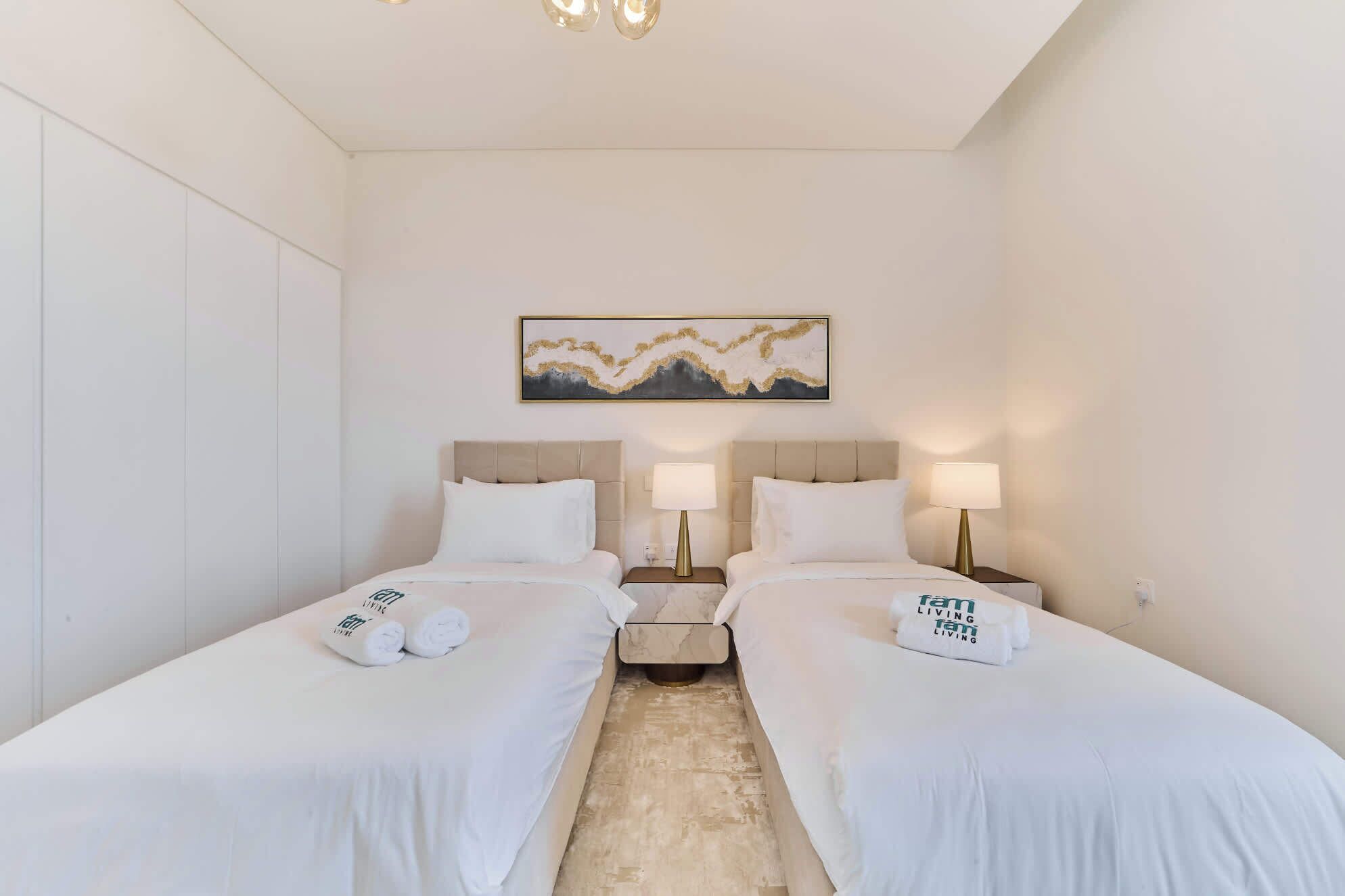 Una habitación de hotel con dos camas, cada una con cabecero, mesitas de noche, lámparas y toallas.