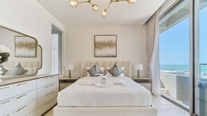 Un dormitorio moderno con una cama grande, mesitas de noche, un aparador y vista al mar.