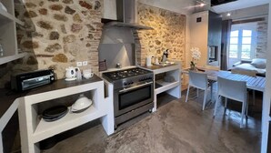 A rustic kitchen with a stone wall, a gas stove, oven, and a small dining area with a table and chairs. - Papillon - Large 90m² apartment in the magnificent village of Seillans (Seillans)
