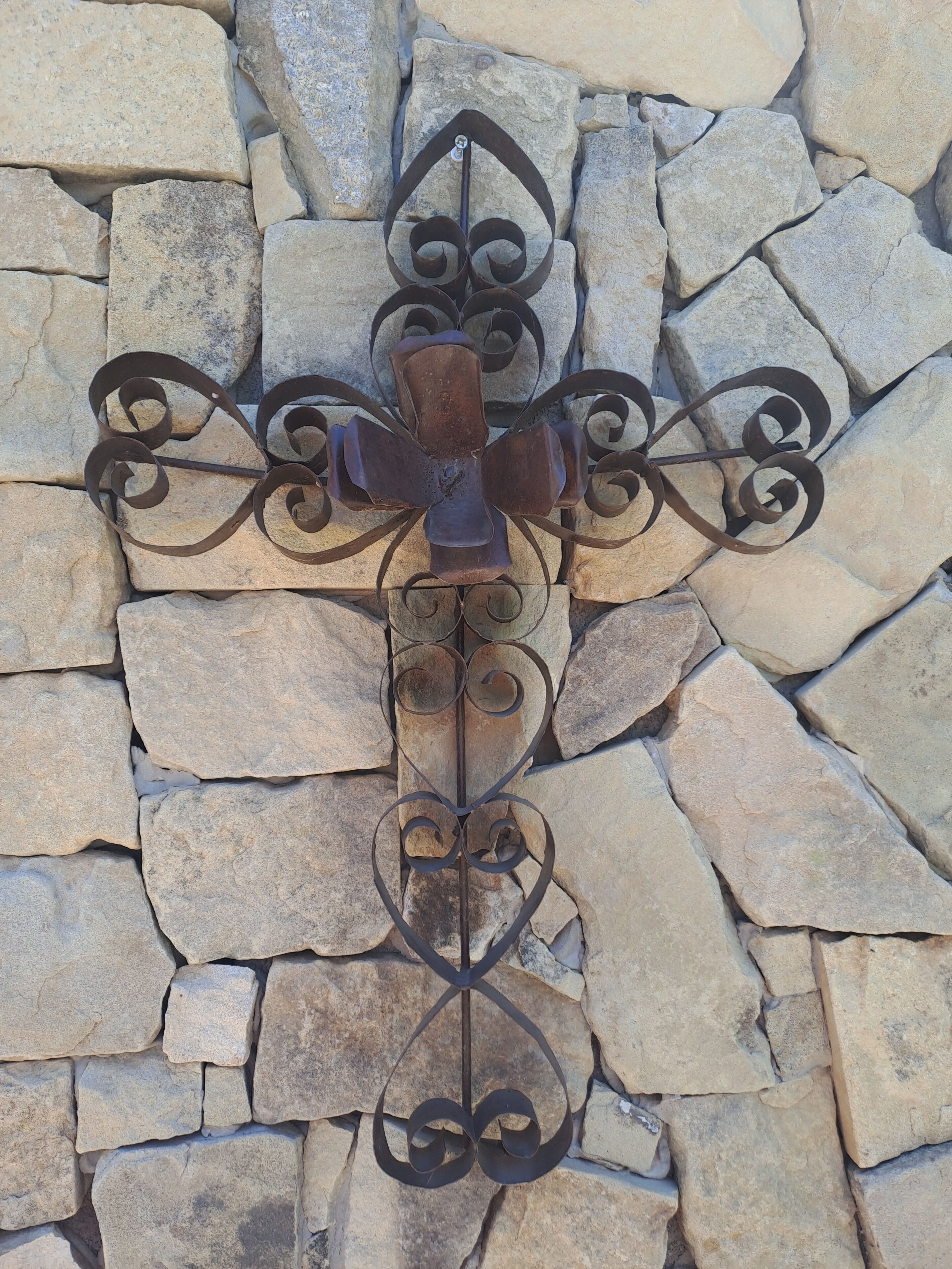 A wrought iron cross mounted on a stone wall.