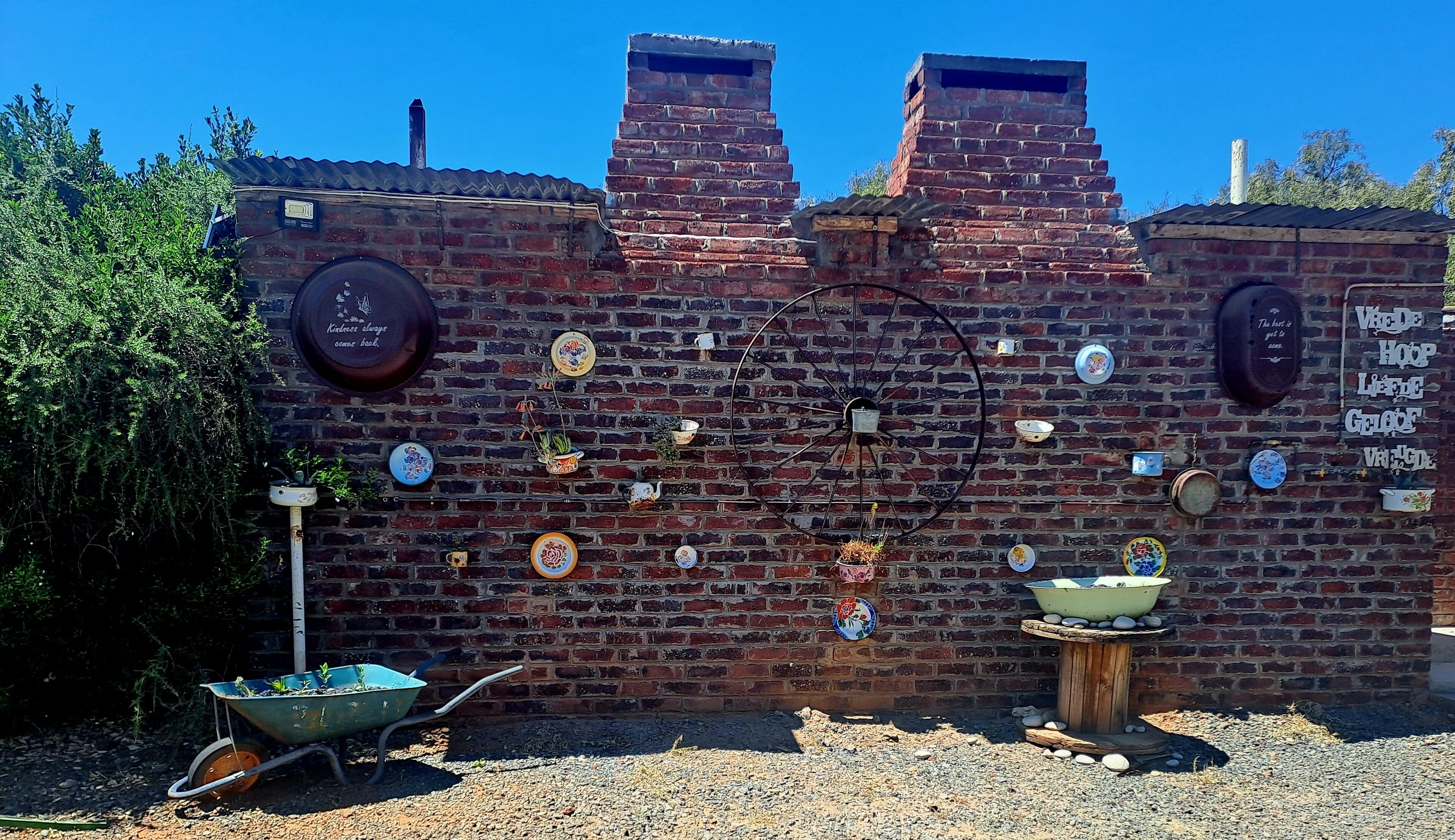 A brick wall with a large wheel, various decorative plates, and a wheelbarrow.
