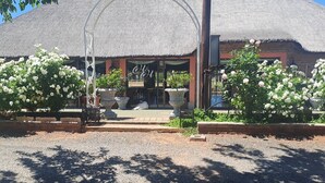 A building with a thatched roof and a sign reading "H&H". There are white flowering plants in front of the building. - SUN DOWN LODGE & CONFERENCE (Maletswai)