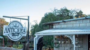 A rustic building with a sign reading "Antiques & Things," featuring a stone facade, a porch with a metal roof, and various items displayed outside. - SUN DOWN LODGE & CONFERENCE (Maletswai)