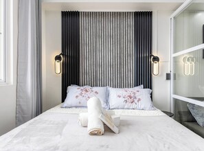 Ein modernes Schlafzimmer mit einem großen Bett, zwei Kissen mit Blumenmuster, einem gerollten Handtuch und einem Nachttisch.