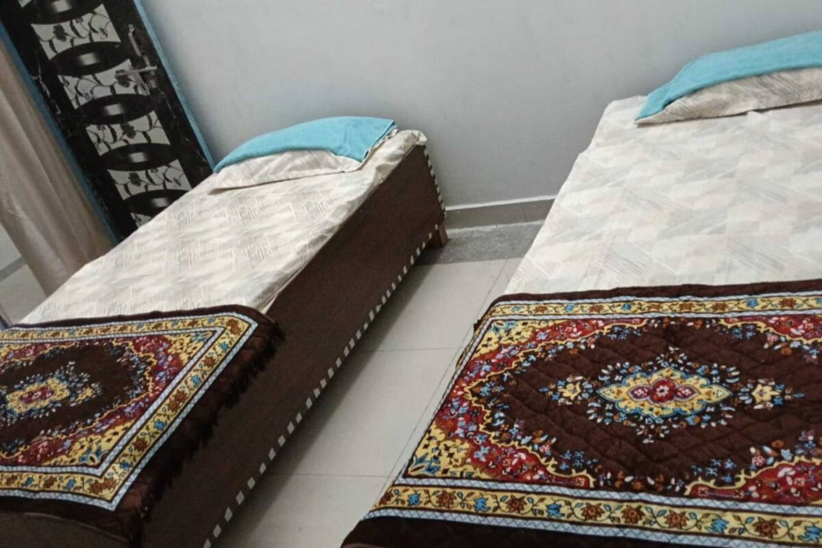 Two beds with patterned bedspreads, a patterned curtain, and a tiled floor.