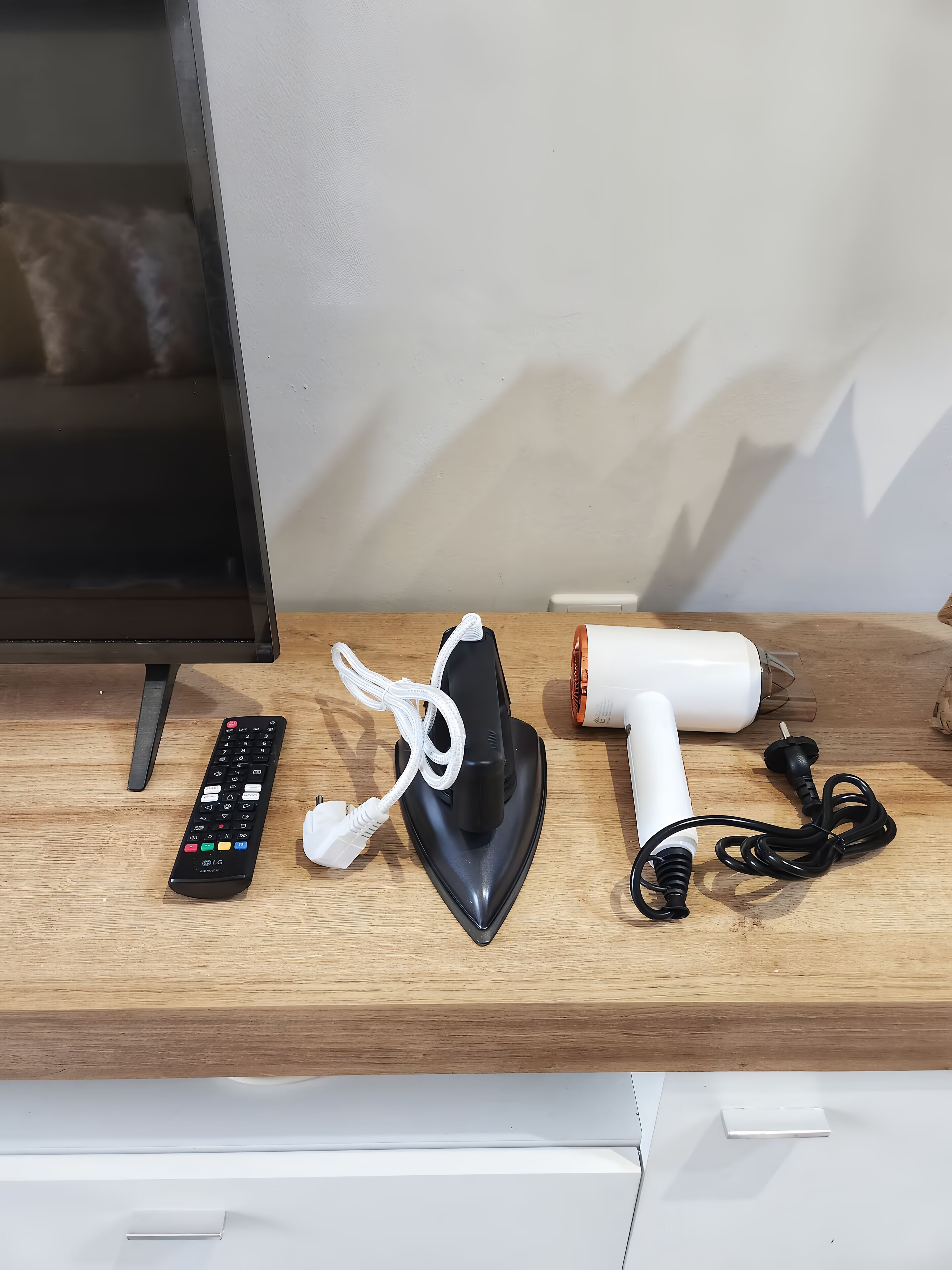 A wooden table with a remote control, a hair dryer, and a curling iron.
