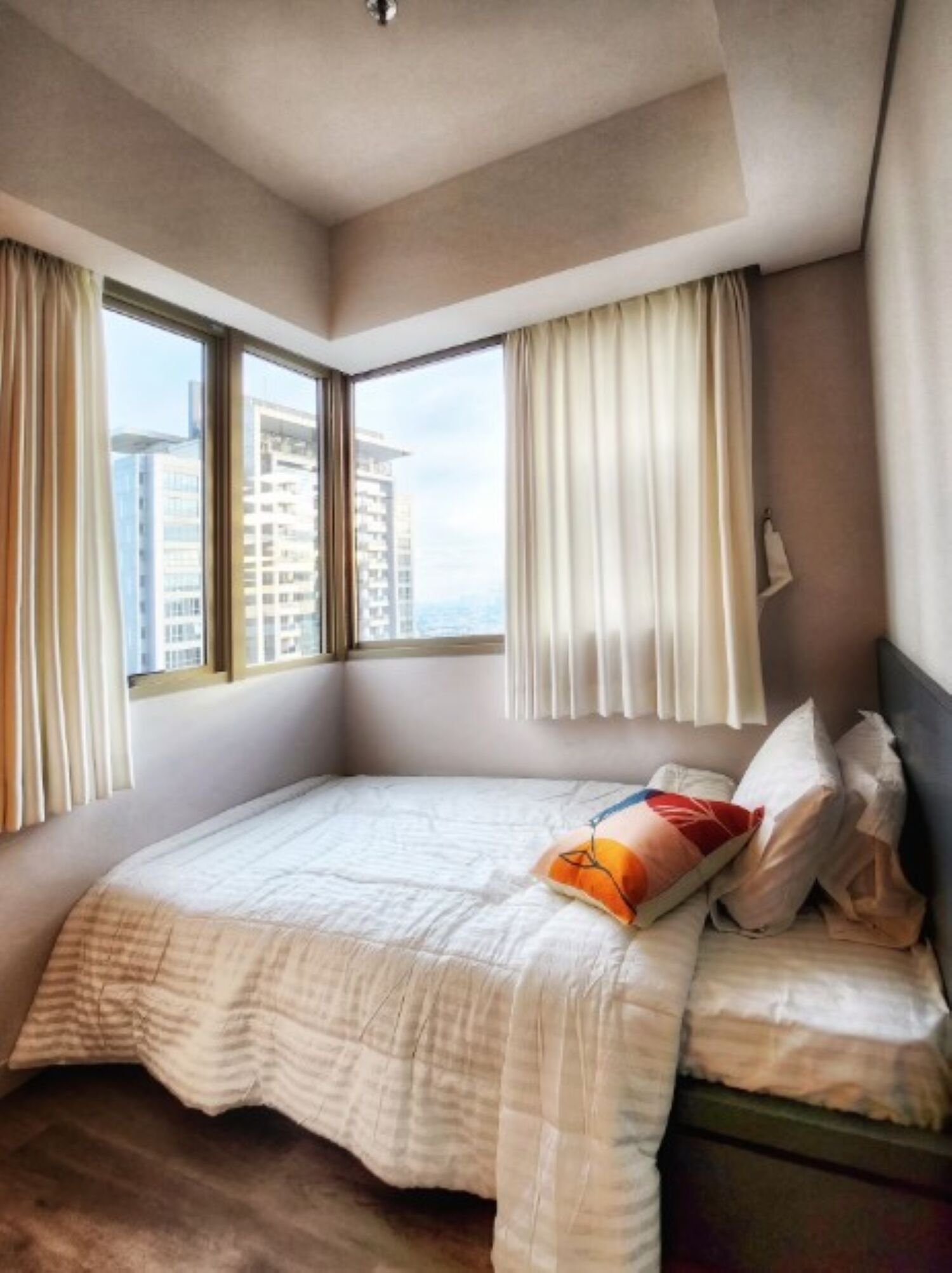 Un dormitorio con una cama grande, dos ventanas y vistas a edificios.