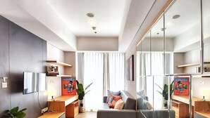 Un salón moderno con sofá, reposapiés y un espejo grande que refleja el ambiente.