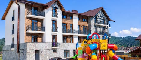 A multi-story hotel with balconies, a playground, and a stone facade.