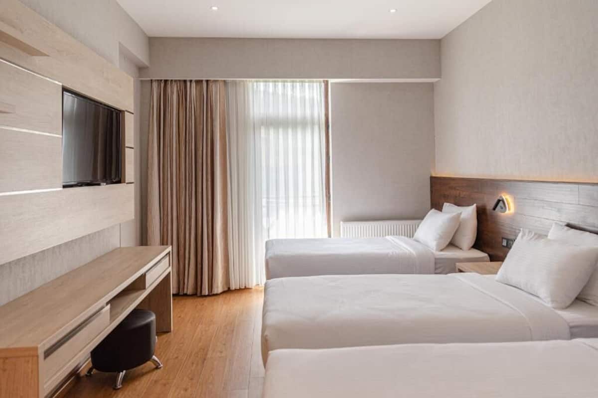 Habitación de hotel con dos camas, un escritorio, un televisor y un ventanal con cortinas.