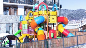 Een speeltuin met glijbanen en klimconstructies, omringd door een hek.