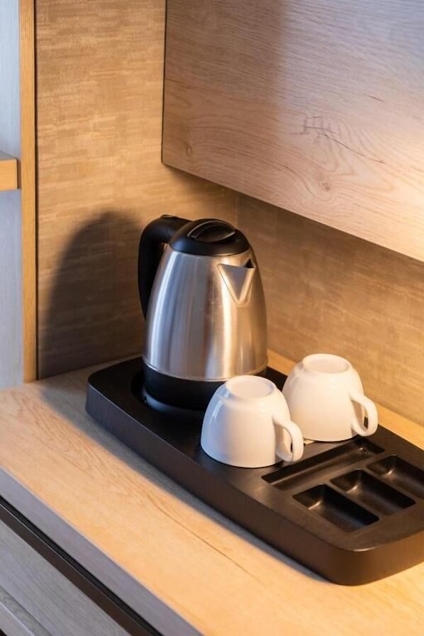 Una tetera eléctrica de acero inoxidable sobre una bandeja negra, con dos tazas blancas a su lado, colocadas sobre una encimera de madera.