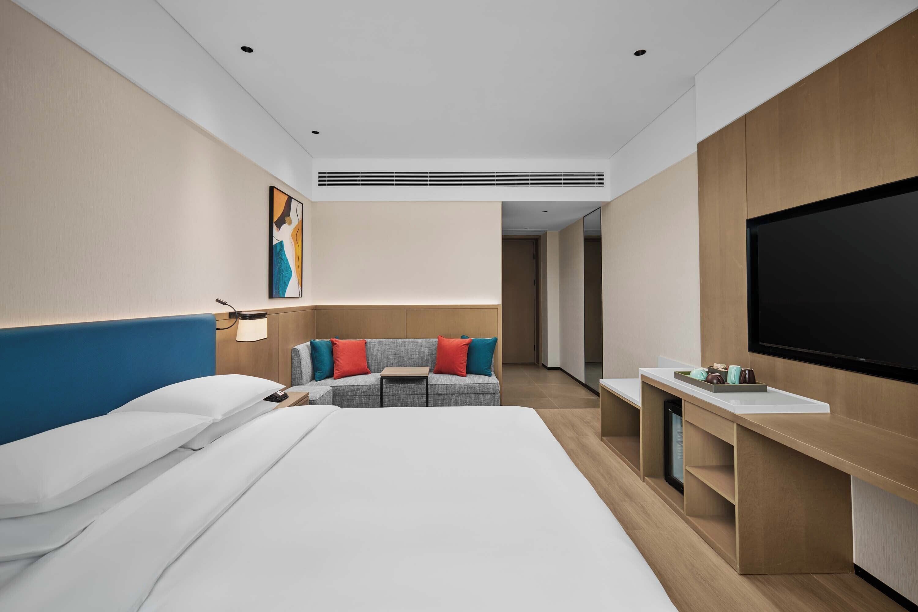 Ein modernes Hotelzimmer mit Bett, Sofa, Fernseher und Schreibtisch.