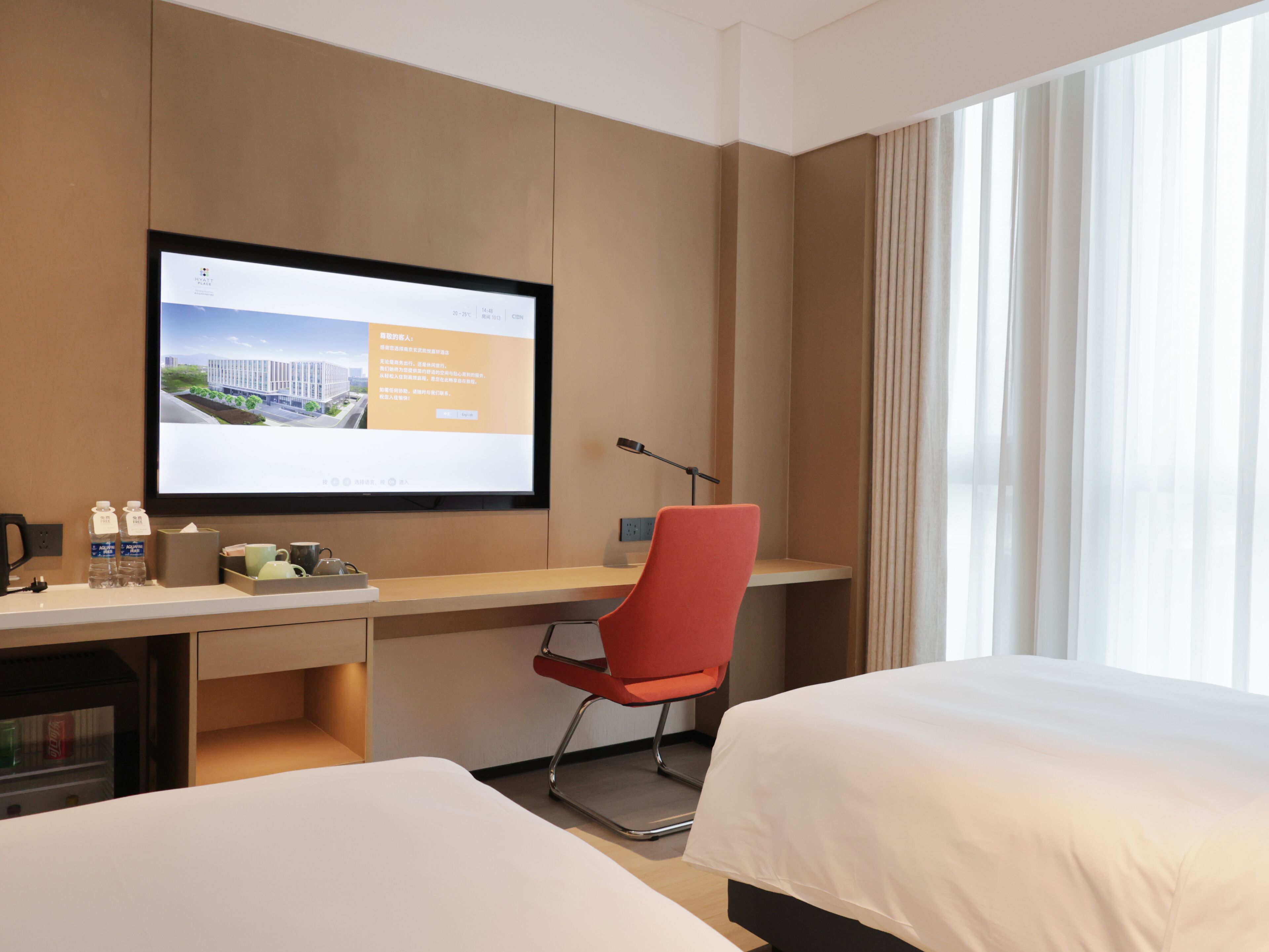 Een hotelkamer met een bureau, twee bedden, een televisie en een raam met gordijnen.