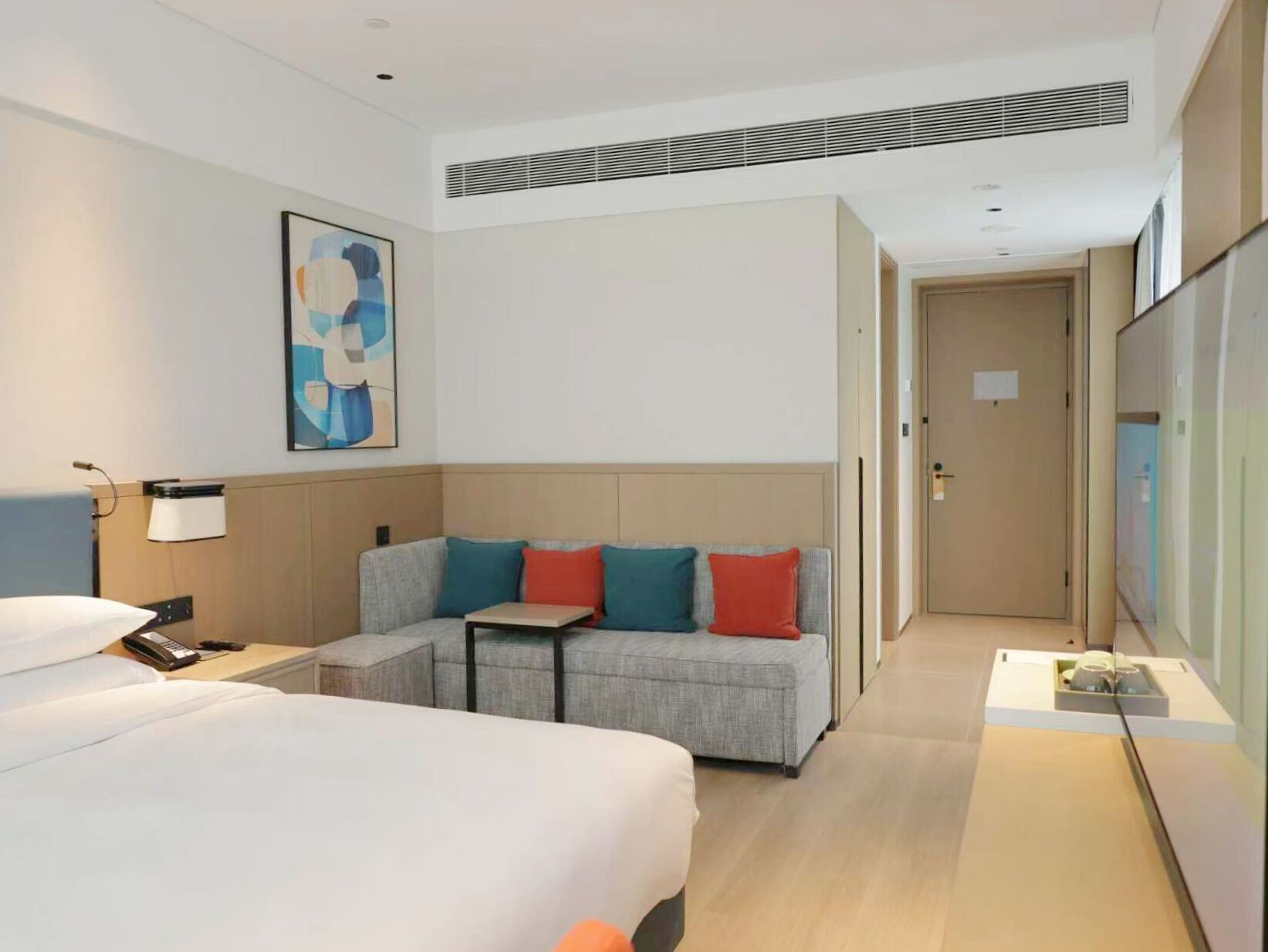 Een hotelkamer met een bed, een slaapbank, een nachtkastje, een lamp en een schilderij aan de muur.