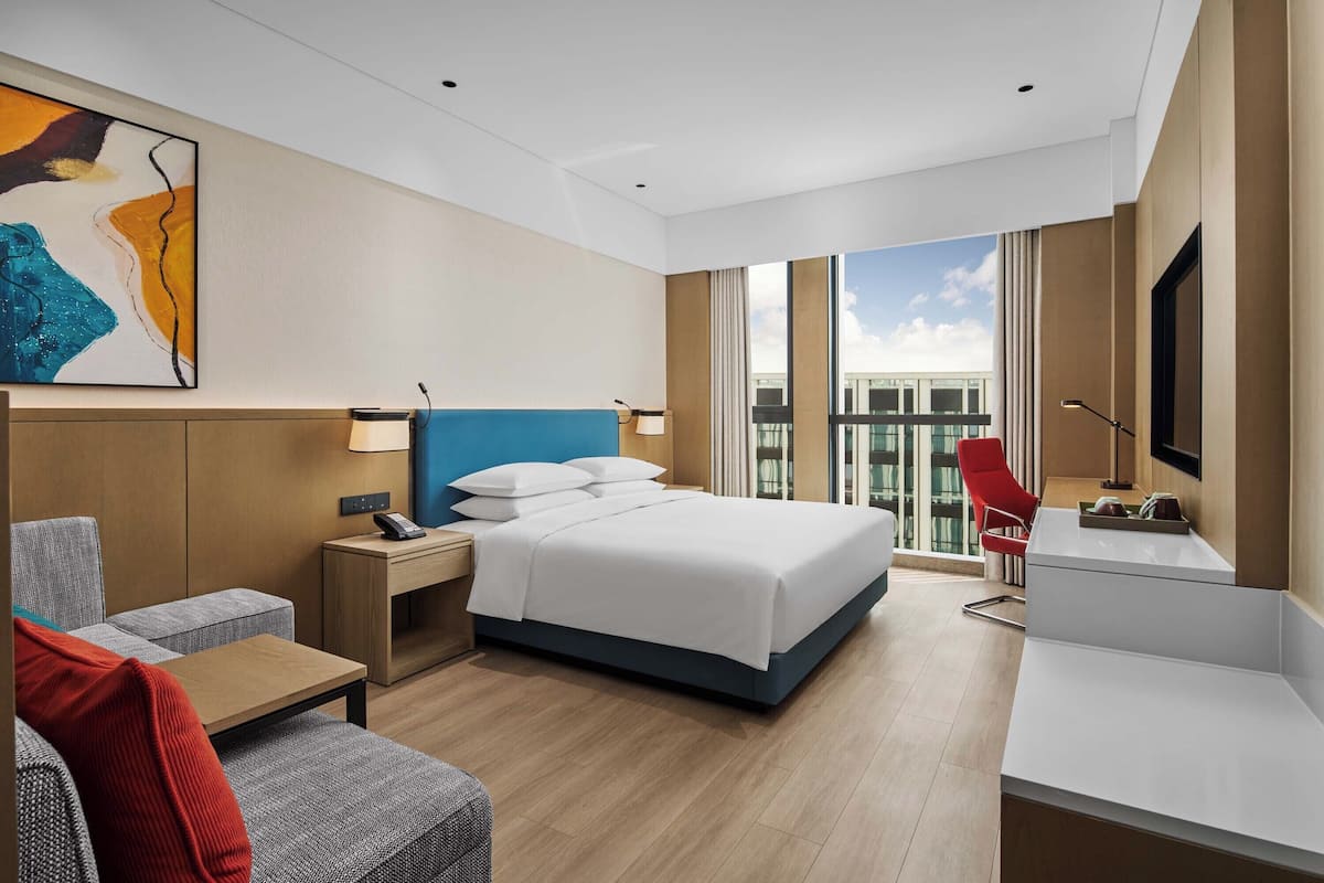 Moderni hotellihuone, jossa on sänky, työpöytä, tuoli, sohva ja suuri ikkuna.