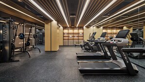 Un gimnàs amb cintes de córrer, aparells de musculació i un mirall gran.