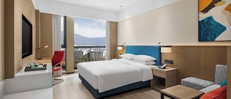 A modern hotel room with a large bed, a desk, a chair, a sofa, and a TV.