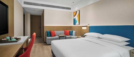 Quarto de hotel com cama, escrivaninha, cadeira, sofá e televisão.