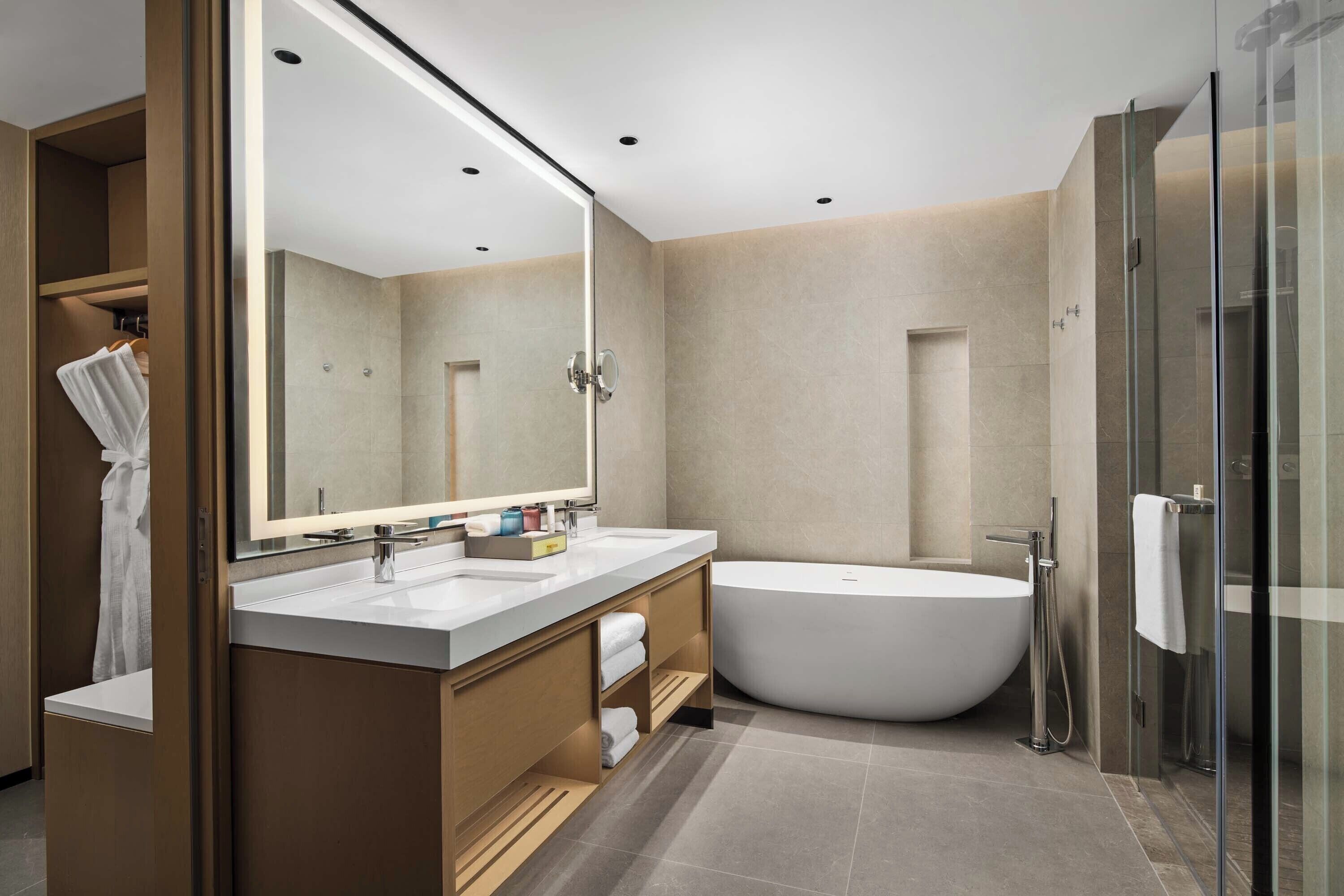 Une salle de bain moderne avec une baignoire sur pieds, deux vasques, un grand miroir et une douche à l’italienne.