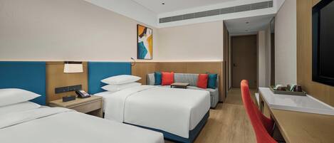 Une chambre d’hôtel avec deux lits, un bureau, une chaise, une télévision et un tableau au mur.