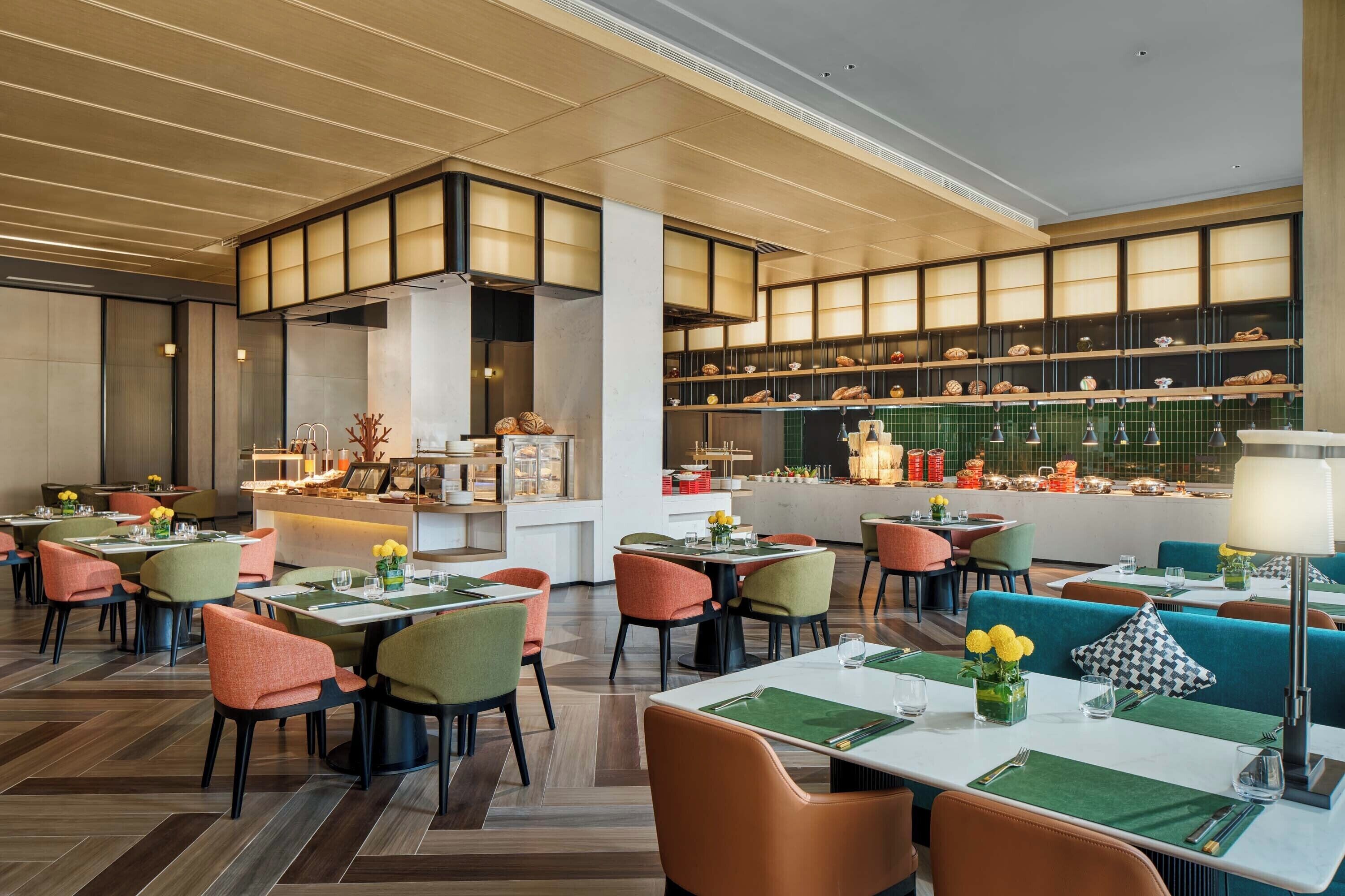 Un ristorante moderno con un bancone centrale, diversi tavoli con sedie e una zona cucina visibile sullo sfondo.