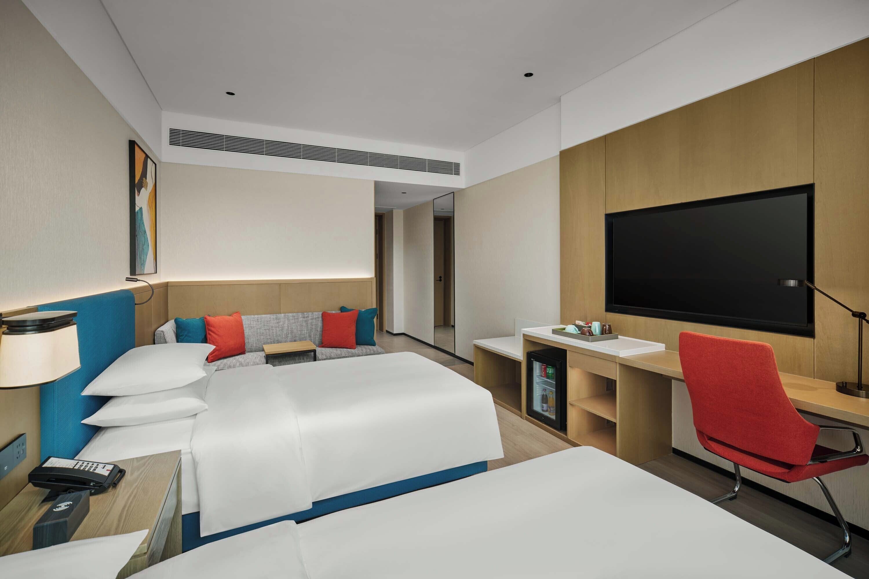 A hotel room with two beds, a desk, a chair, a TV, and a minibar.