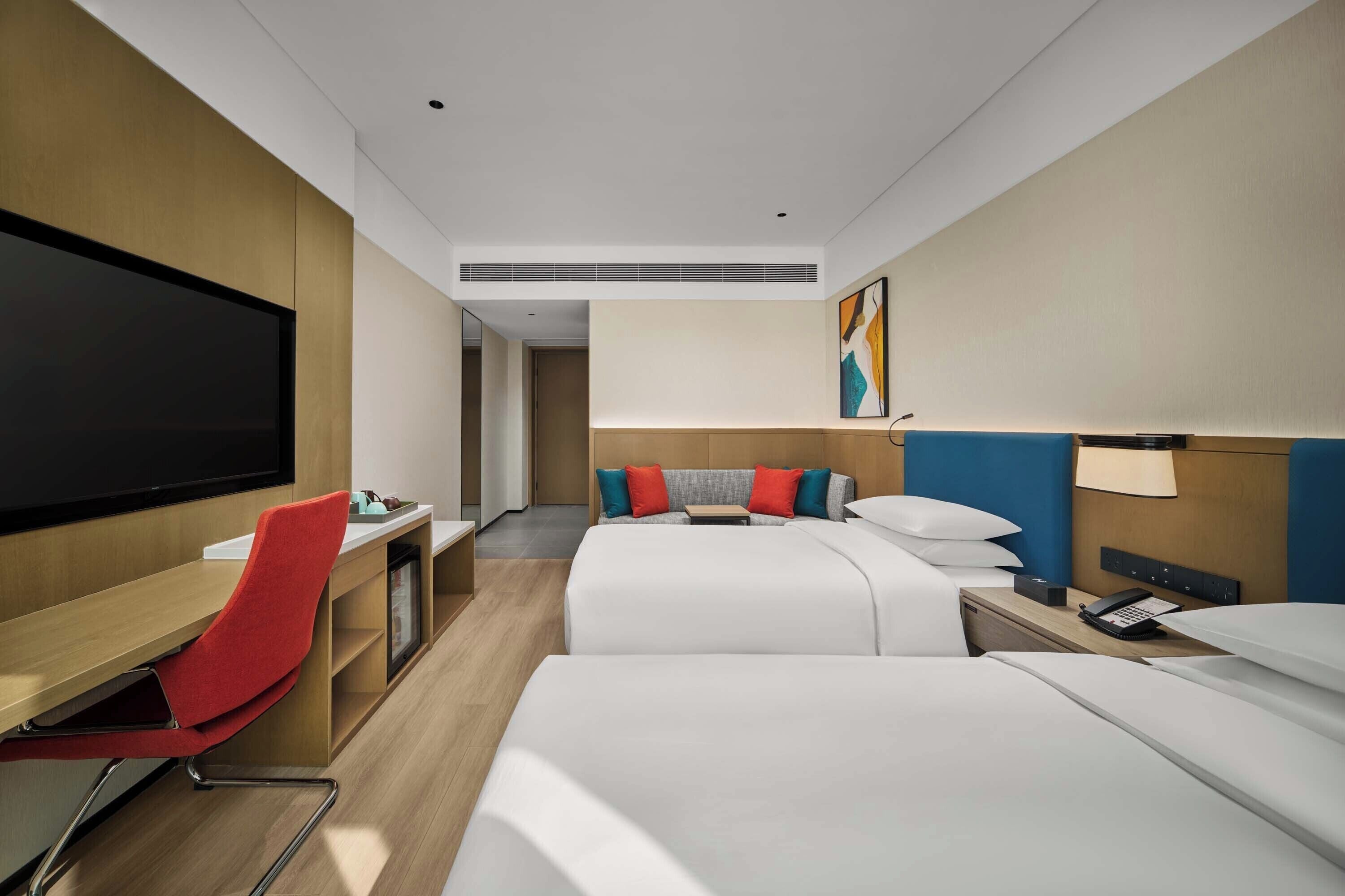 A hotel room with a TV, two beds, a desk, and a chair.