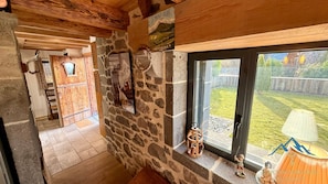 A rustic interior with stone walls, wooden beams, and a view of a backyard.