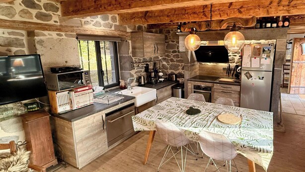 Una cocina rústica con paredes de piedra, vigas de madera, una isla grande y electrodomésticos modernos.