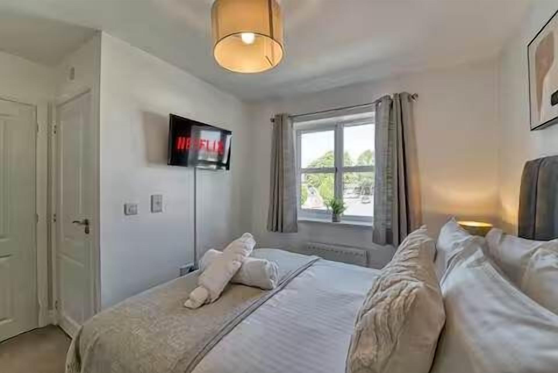 A bedroom with a bed, a TV mounted on the wall, a window with curtains, and a door.