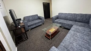 Ein Wohnzimmer mit zwei grauen Sofas, einem Glastisch und einem dunklen Holznachttisch mit elektronischen Geräten.