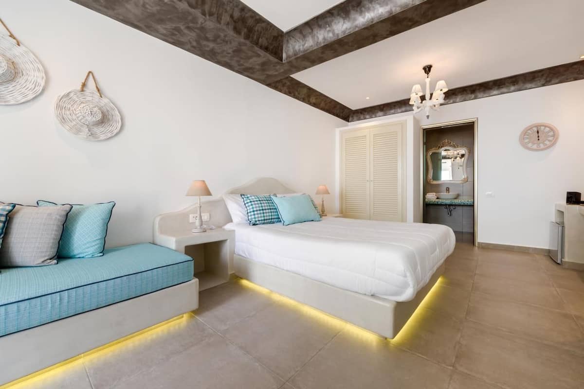 A bedroom with a bed, bedside tables, a sofa, a chandelier, and a mirror.