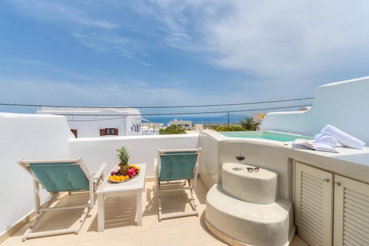A rooftop terrace with two lounge chairs, a small table with fruit, a hot tub, and a view of the sea.