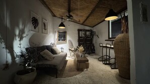 A cozy living room with a sofa, a coffee table, and a large potted plant. There is a ceiling fan, a window with a view, and a wicker chair. - A refuge for two between orchard and sea in Valencia, located in P.N.de lálbufera (Valencia)