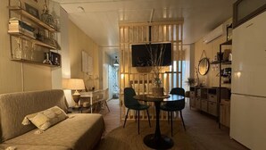 A cozy living room with a sofa, a dining table with chairs, a TV, and a kitchen area with a refrigerator. - A refuge for two between orchard and sea in Valencia, located in P.N.de lálbufera (Valencia)