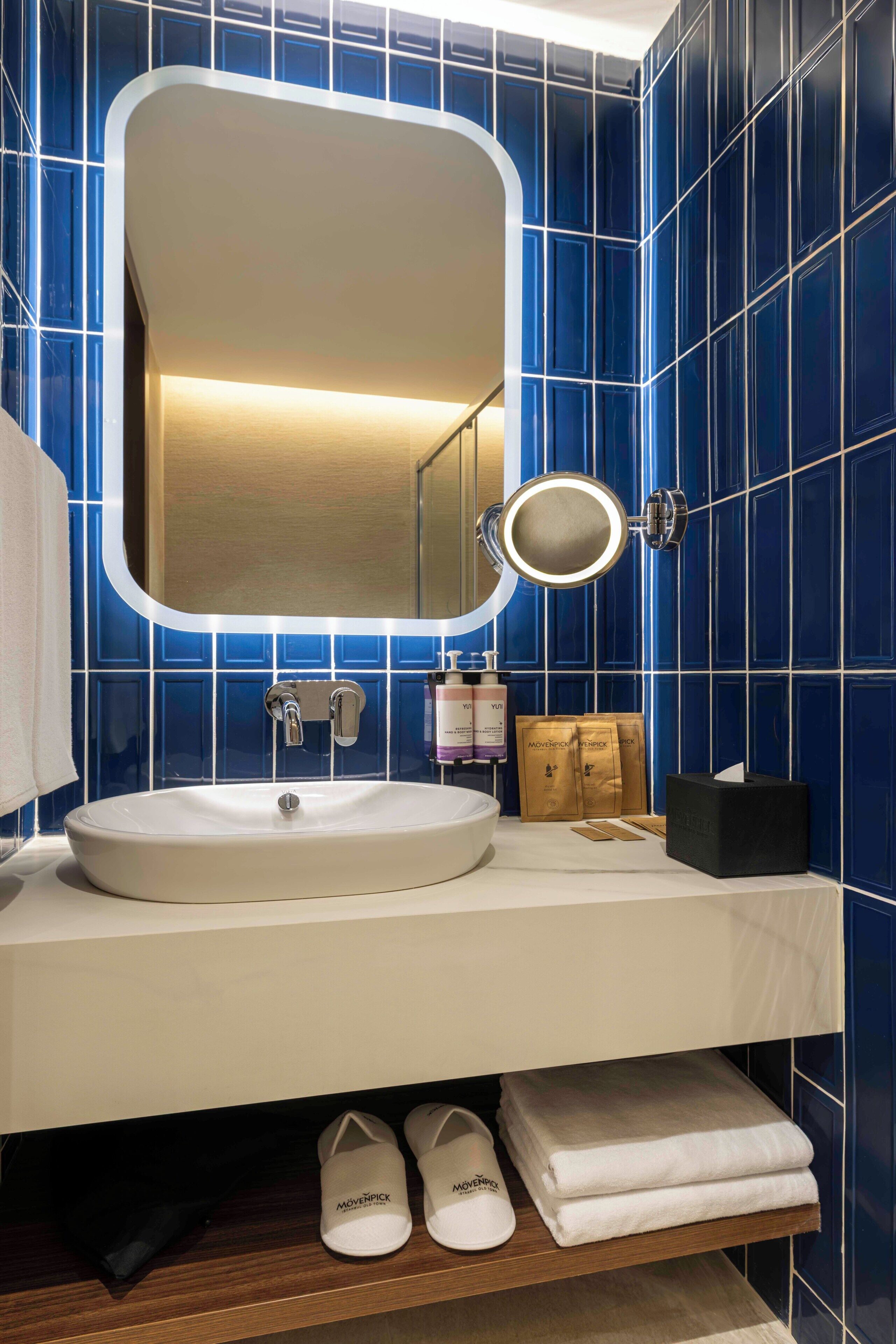 A bathroom with a white sink, a mirror with a light, and blue tiles.