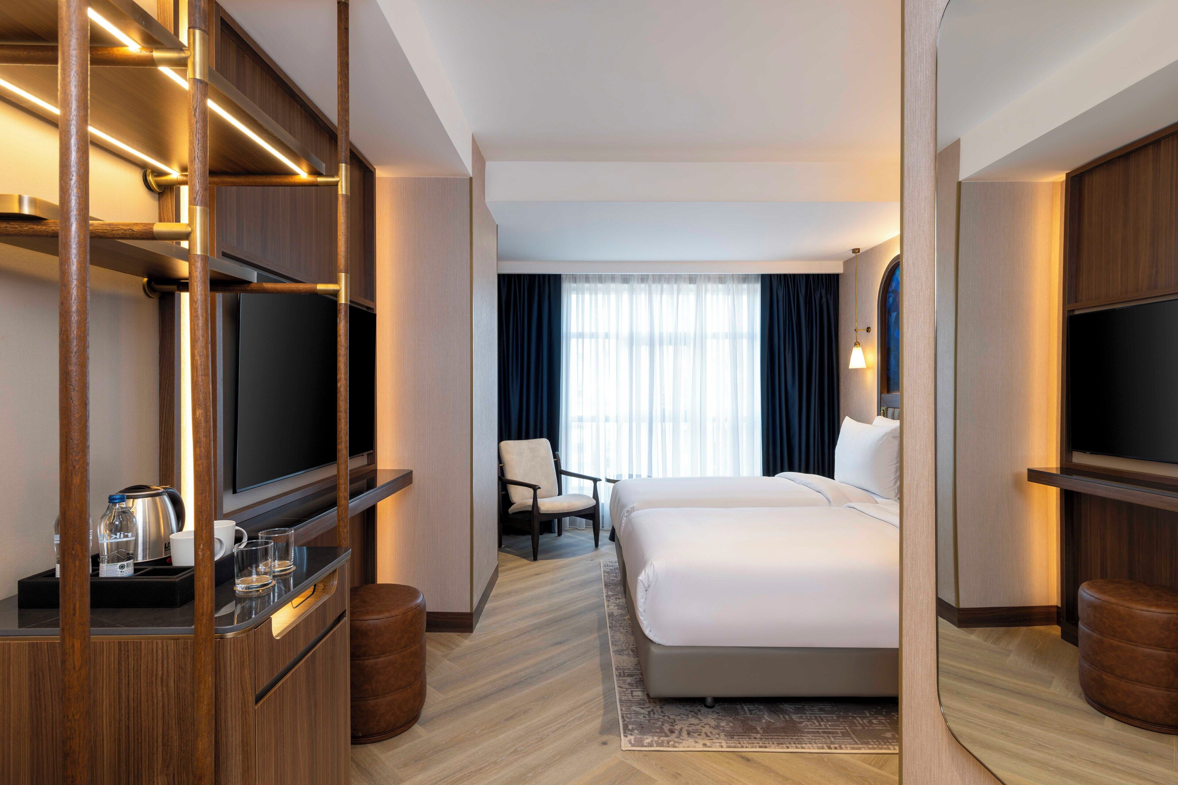 Ein Hotelzimmer mit einem großen Bett, einem Fernseher, einem Schreibtisch mit Wasserkocher und einem Sessel.