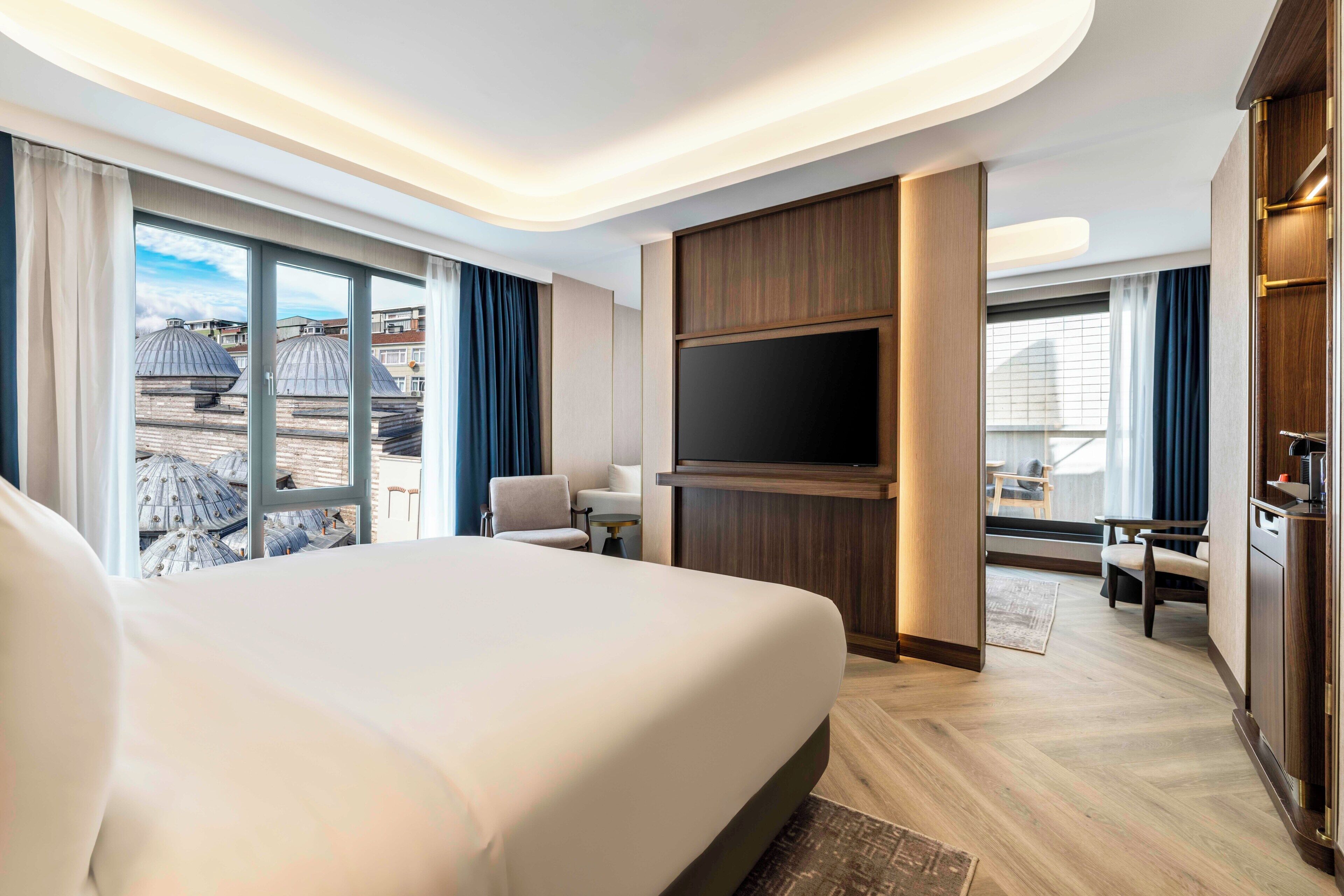 A hotel room with a large bed, a TV, a desk, and a view of the cityscape.