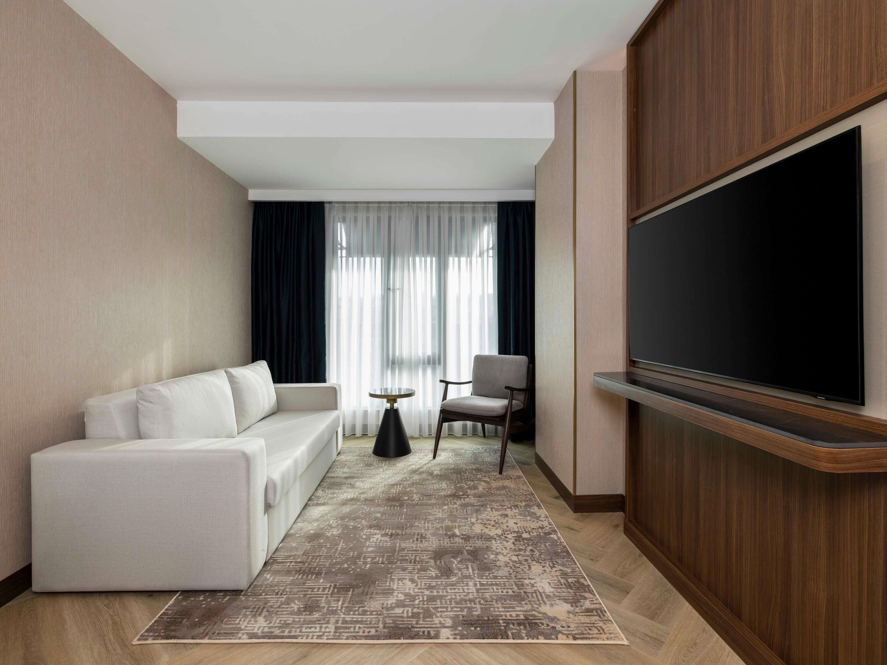 Una camera d'albergo moderna con un divano, una TV, un tavolino e una sedia.