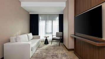 Una camera d'albergo moderna con un divano, una TV, un tavolino e una sedia.