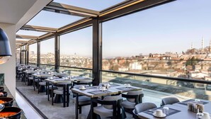 A rooftop restaurant with tables and chairs, large windows, and a city view. - Mövenpick Istanbul Old Town (Istanbul)