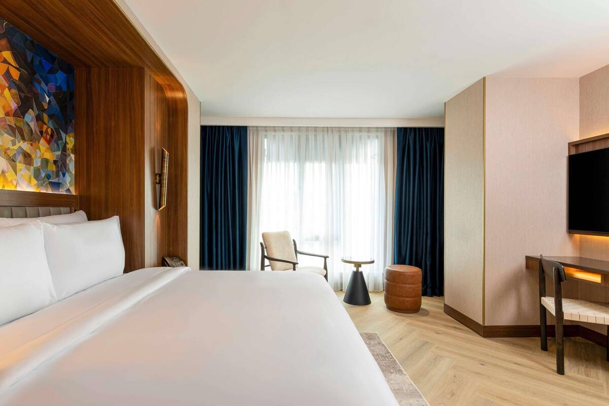 Una habitación de hotel con una cama grande, un escritorio, una silla, una mesita y un televisor.