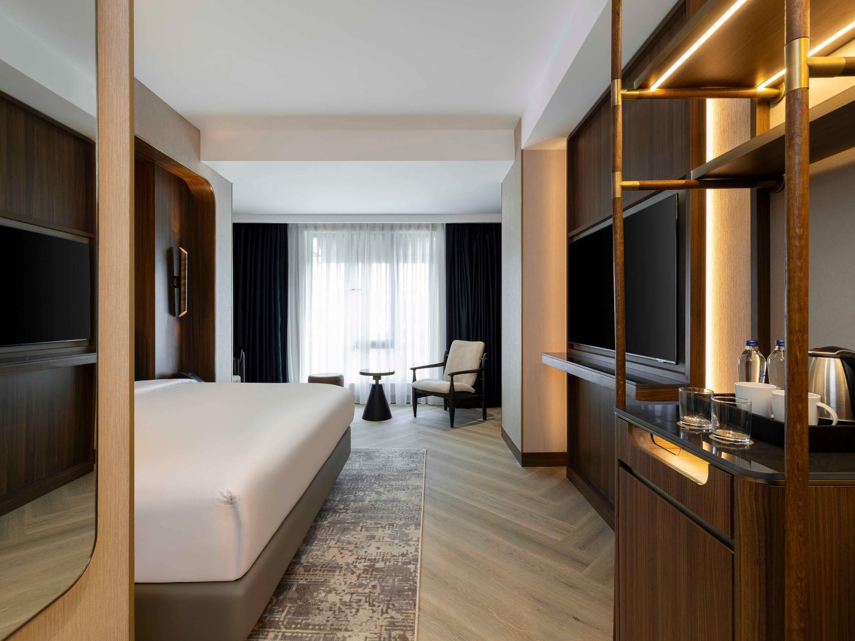 A hotel room with a bed, a desk, a chair, a TV, and a window with curtains.