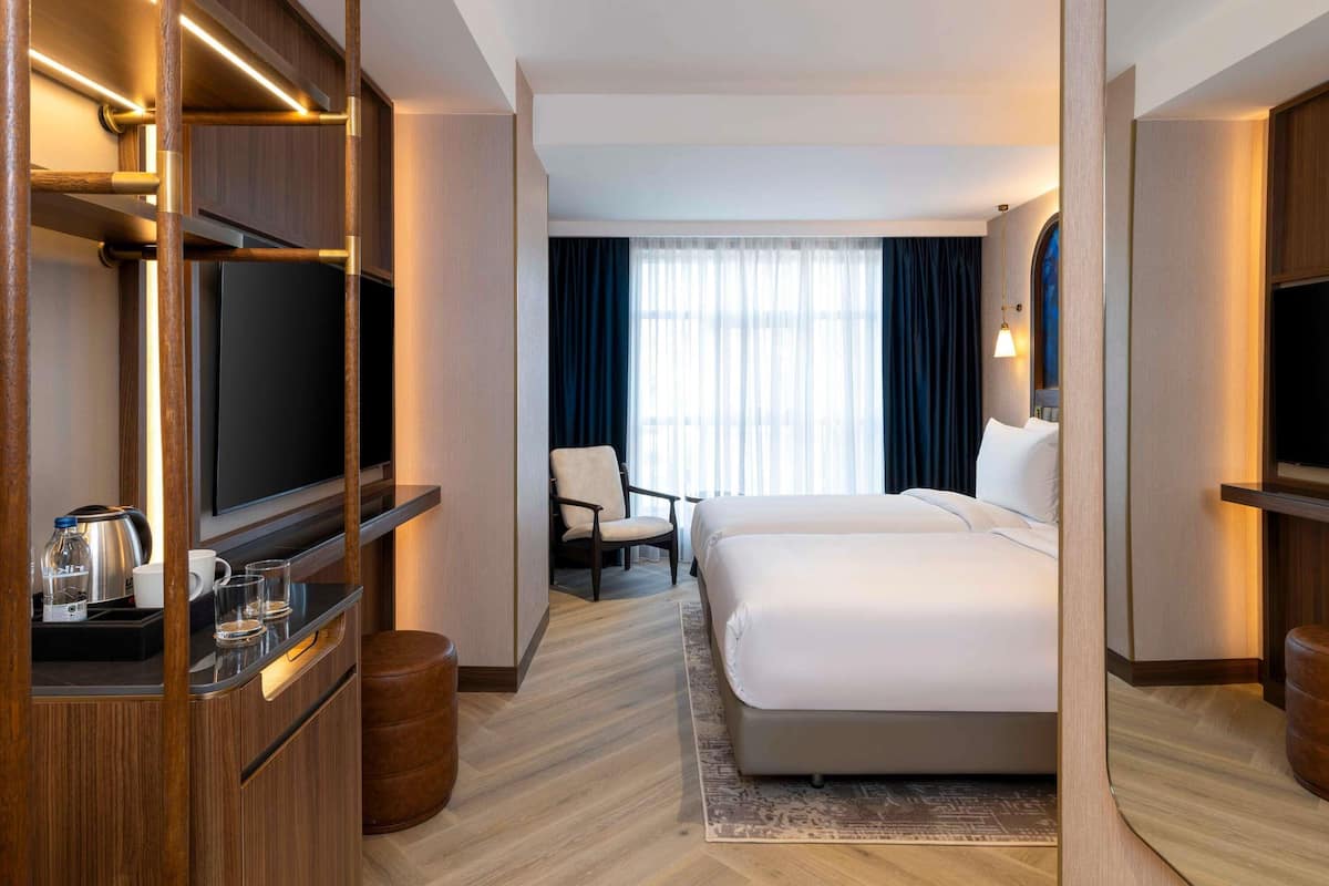 Una habitación de hotel con cama, televisor, escritorio con tetera y una silla.