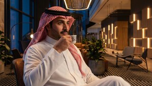 A man in traditional attire sitting in a modern hotel lobby with a large chandelier, seating area, and potted plants. - Novotel Madinah (Madinah)