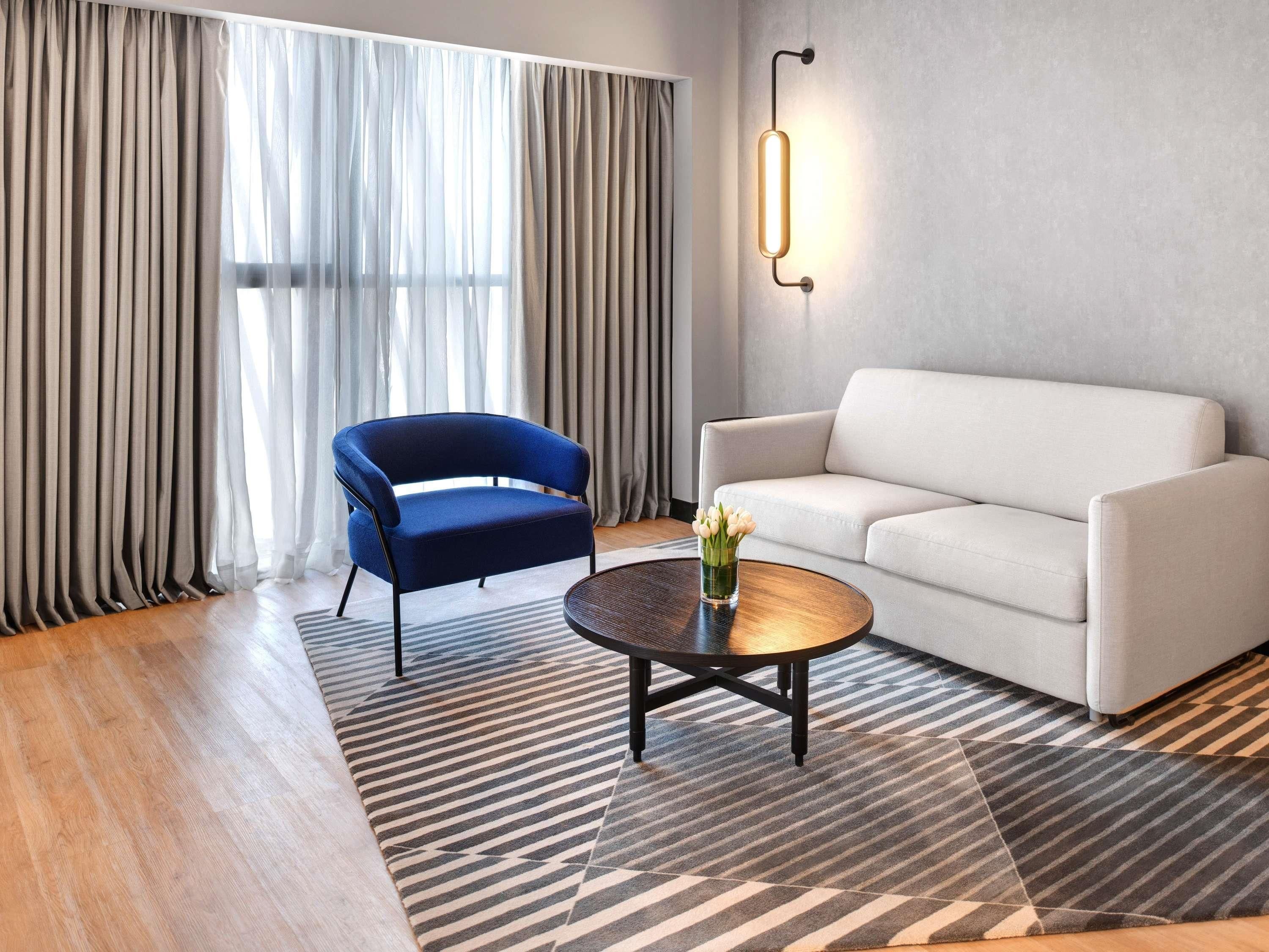 Una sala de estar moderna con un sillón azul, un sofá blanco, una mesa de centro redonda y una alfombra estampada.