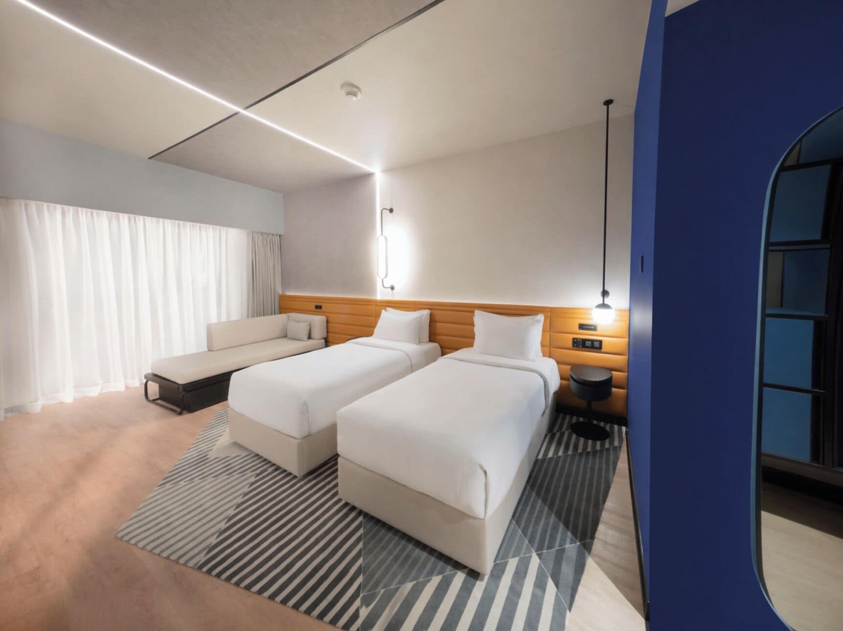 Habitación de hotel con dos camas, un sofá, una mesita de noche, una lámpara y vistas al exterior.