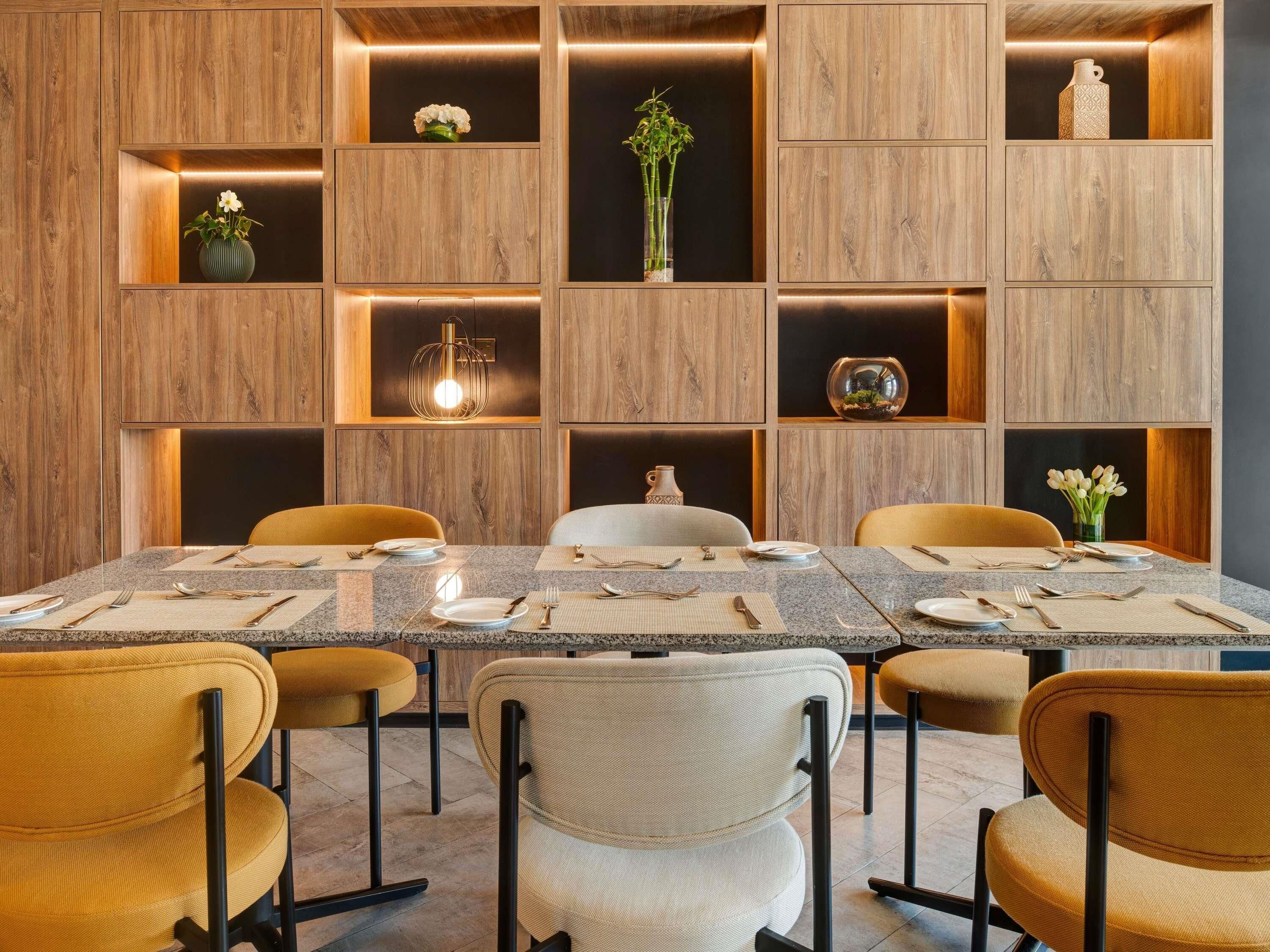 A modern dining area with a rectangular table, six chairs, and built-in wooden shelves with decorative items.